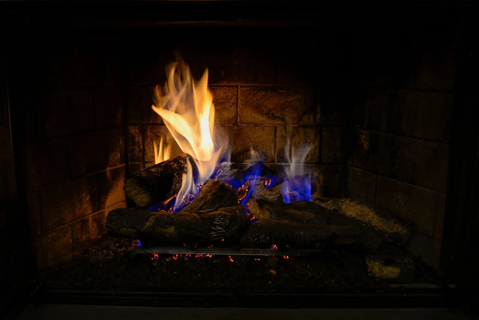 Gas log set burning with blue and orange flames inside a dark firebox