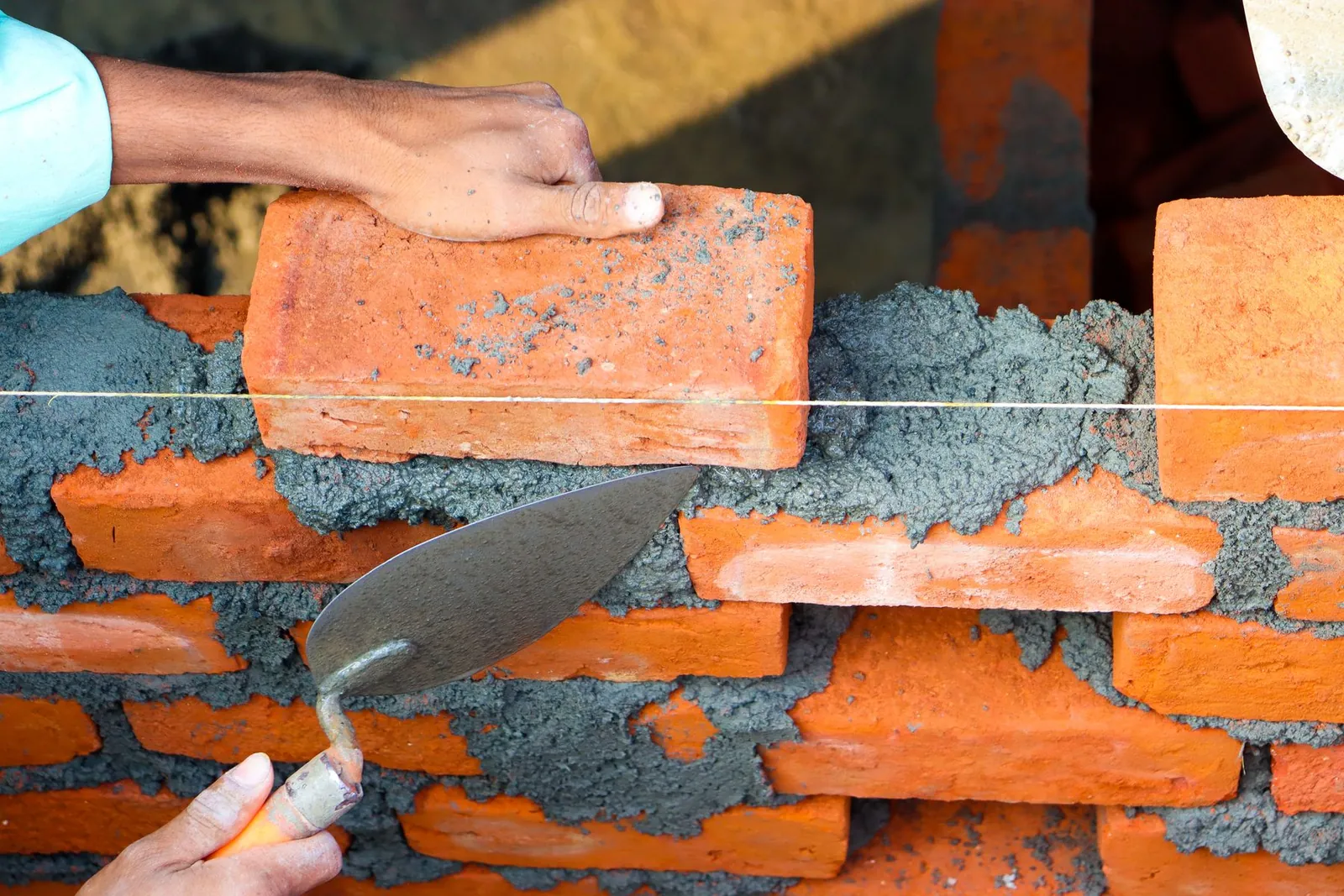 Hands setting a red brick into fresh mortar with a steel trowel and line