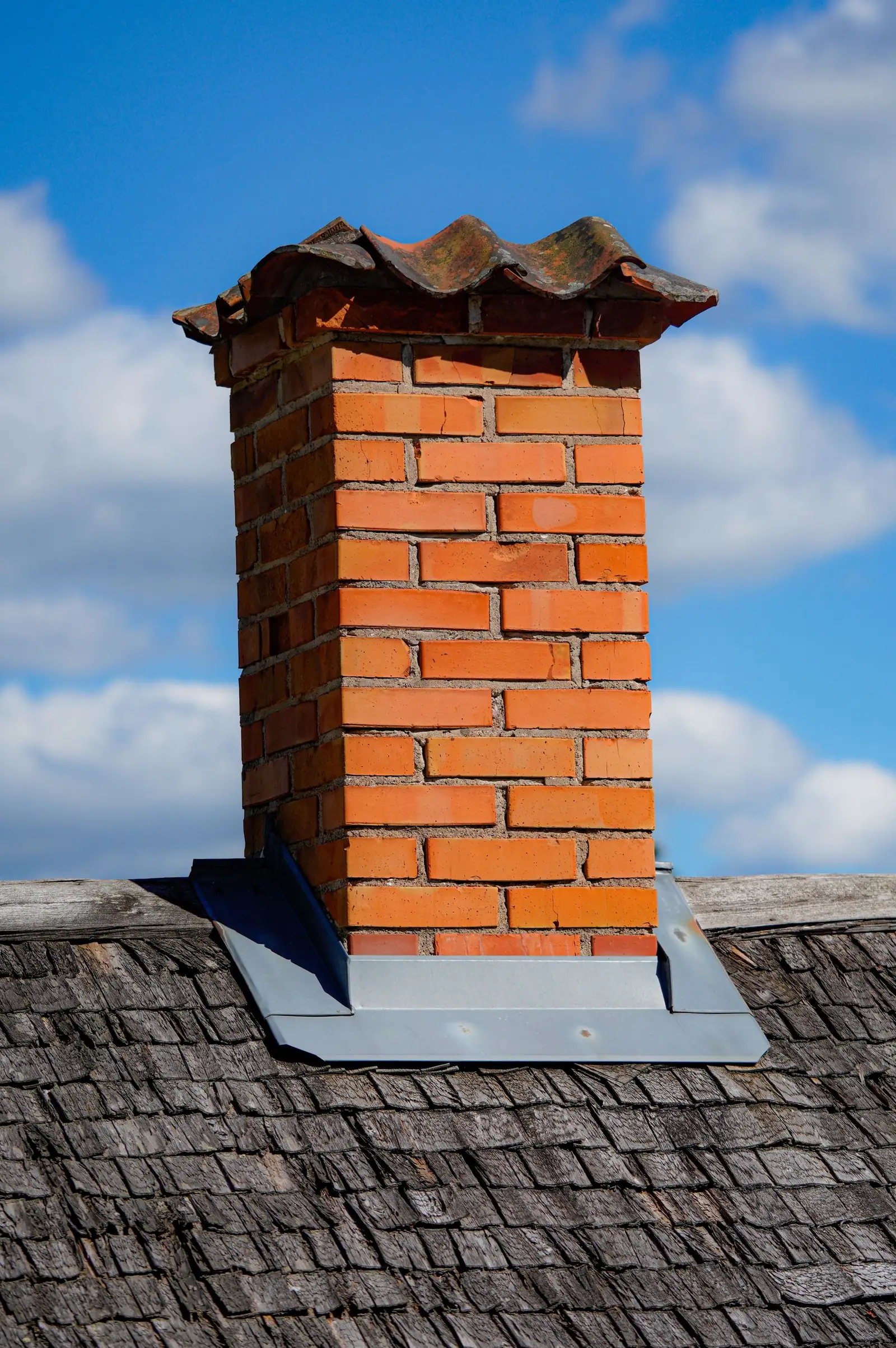 Orange brick chimney with metal step flashing on a weathered cedar shingle roof