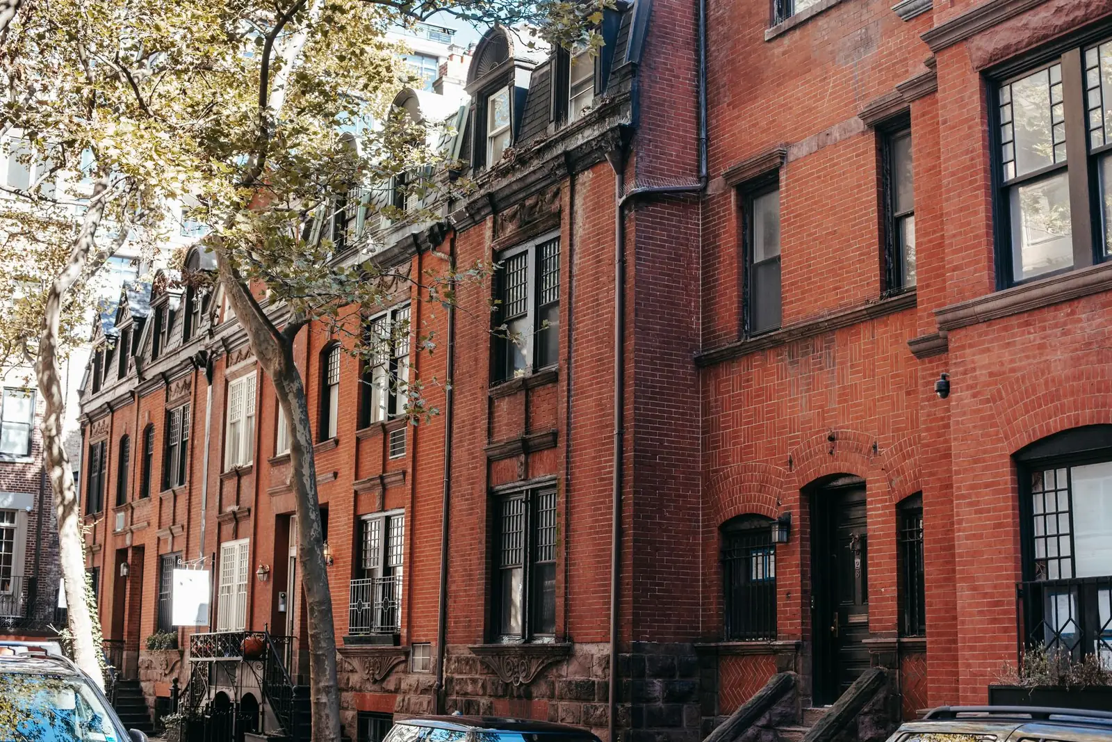 Sunlit block of red brick row houses with stoops and tall sash windows