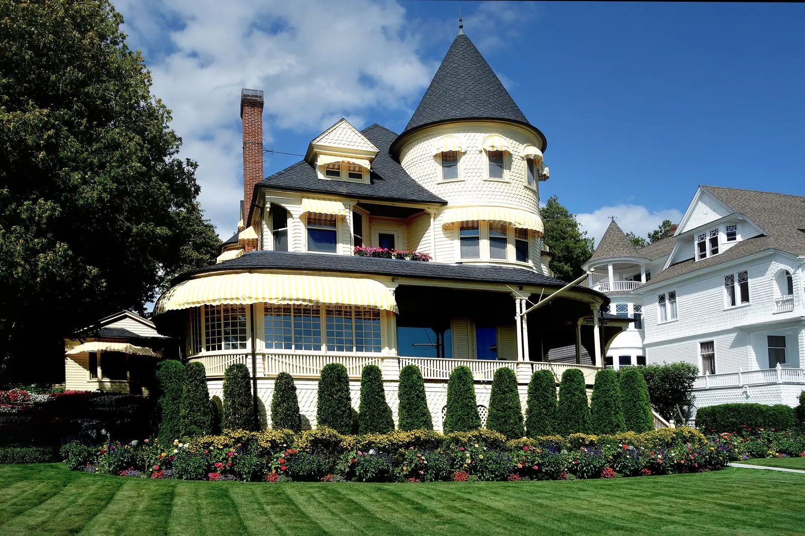 Cream Queen Anne Victorian with a turret, striped awnings and a tall brick chimney