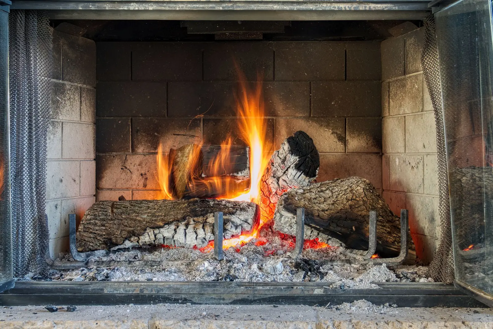 Split oak logs burning on a grate inside a firebrick-lined masonry fireplace